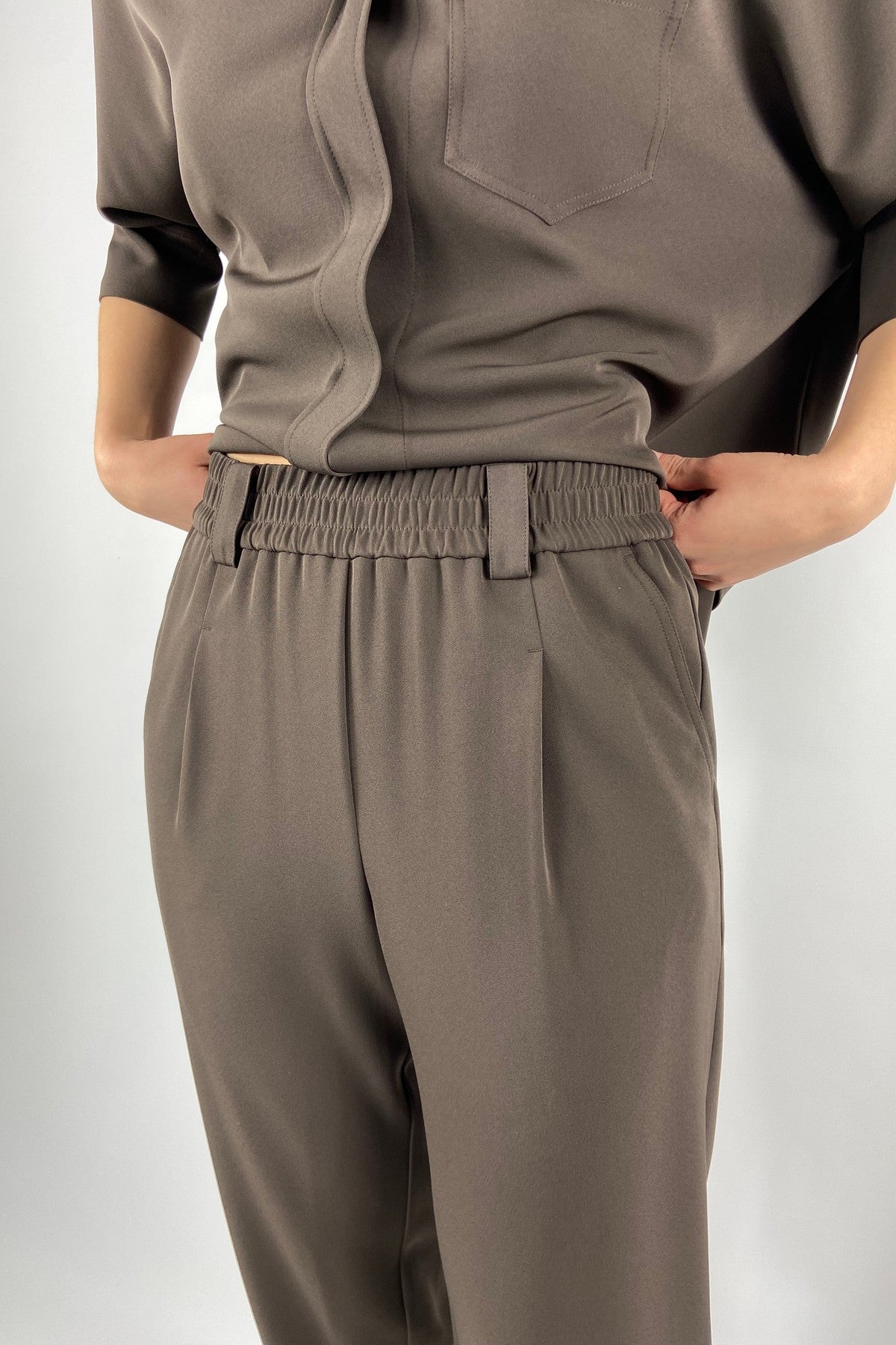 15473 Detail van FFC broek in bruine vloeiende stof met steekzakken en riemlussen.