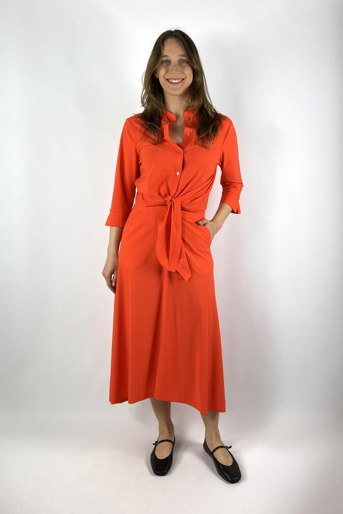 456L Nineto9 shirtbloes in de kleur Aperol met 3/4 mouwen en strikdetail onderaan van travel-kwaliteit.