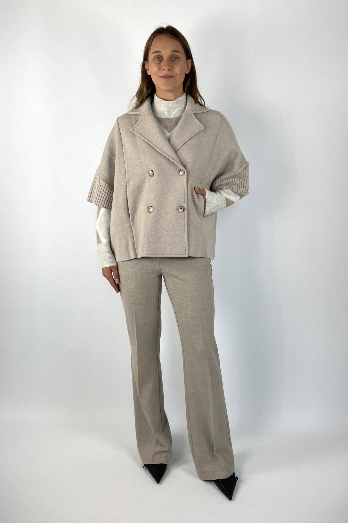 Luxueuze korte gebreide vest met dubbele rij schelpknopen in lichtbeige. De mouwen zijn halflang.