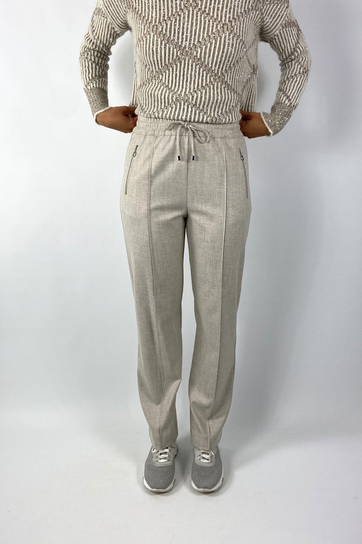 Beige broek met elastische tailleband en stropje voorzien van 2 steekzakken met rits. 