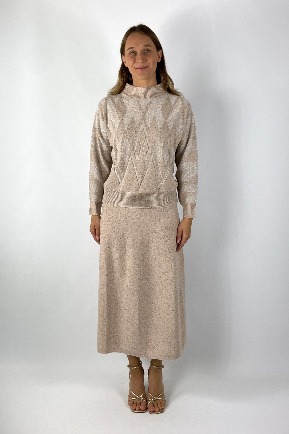 Lange rok in tweed stof. De kleur is beige-roze. Mooit te combineren met de bijpassend trui met ruit.