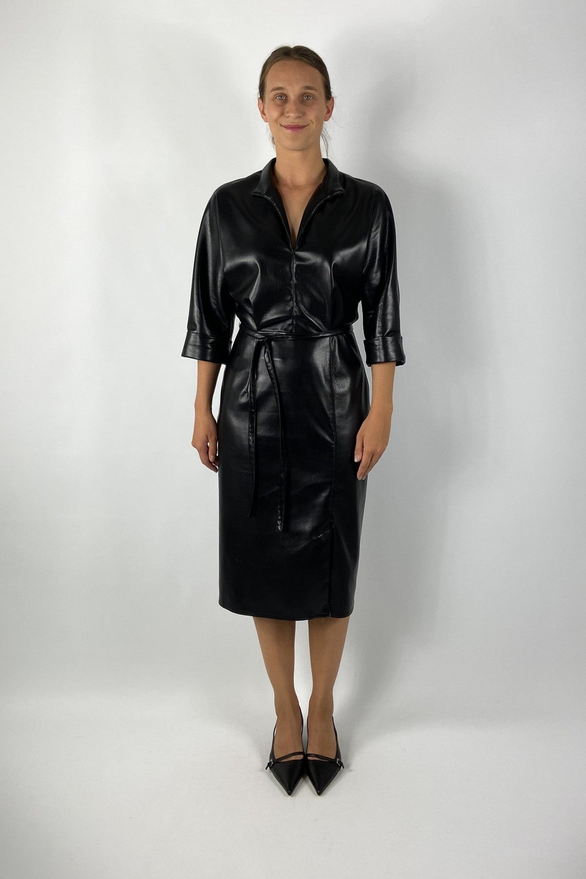 De zwarte Djana-jurk van Natan in imitatieleer heeft een glanzende finish, slank silhouet en soepele rok – elegant met moderne allure.