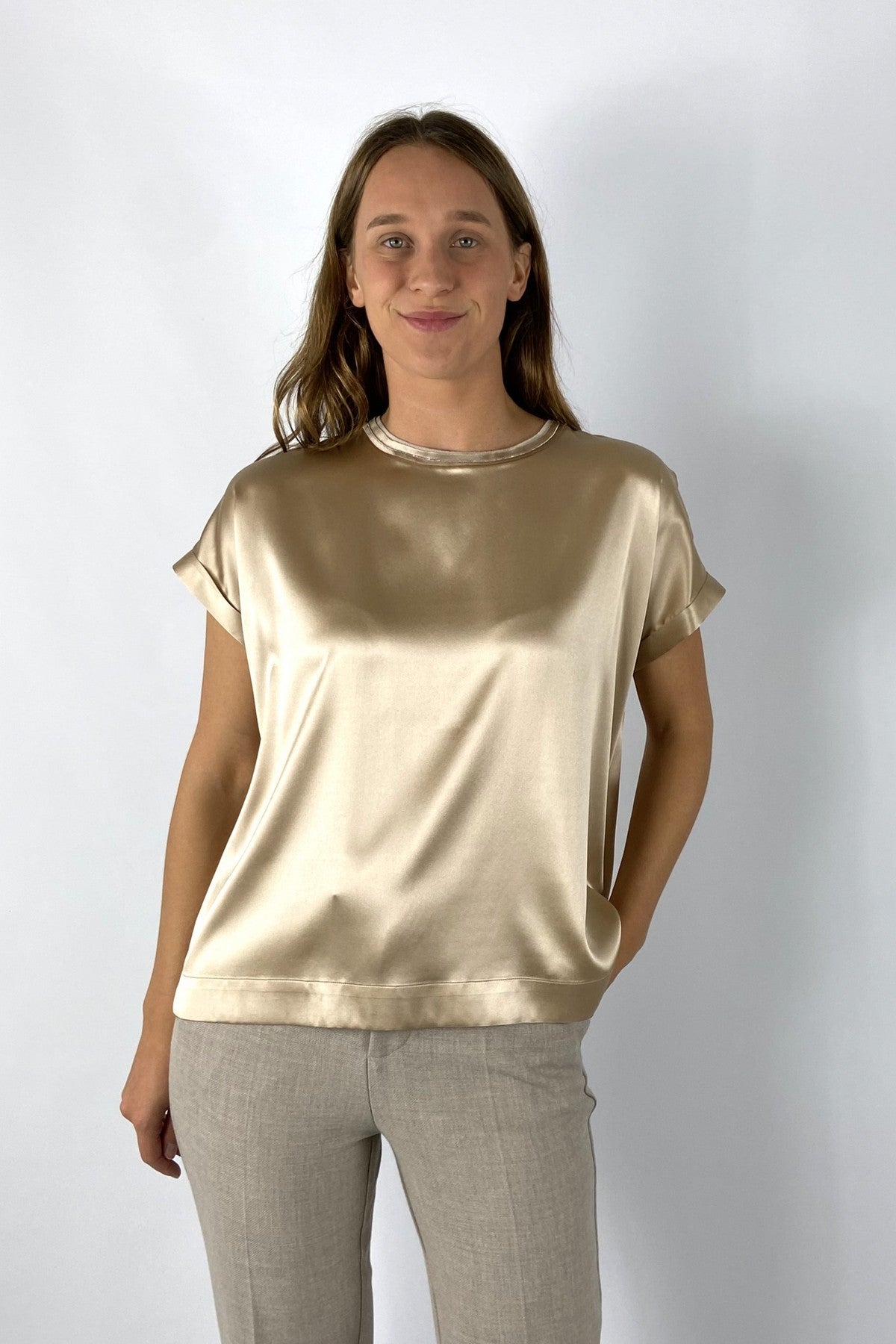 Een glanzend  amberkleurig dames-T-shirt in zijde satijn met korte, wijde kimonomouwen. Aan de halslijn schittert een subtiel glinsterend detail. De snit is losjes met een licht uitlopende zoom.